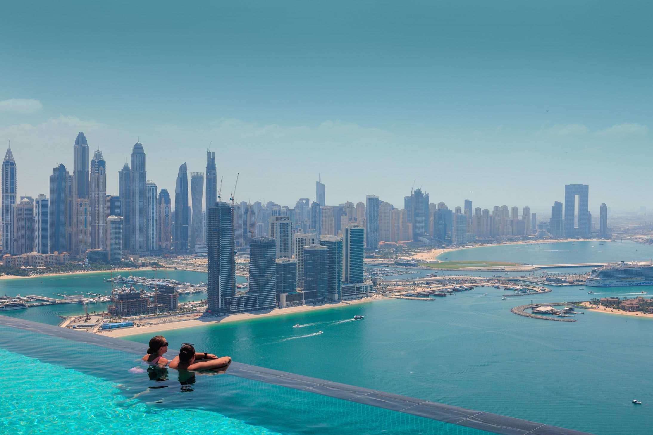 Two women in a rooftop infinity pool overlooking the Dubai skyline.